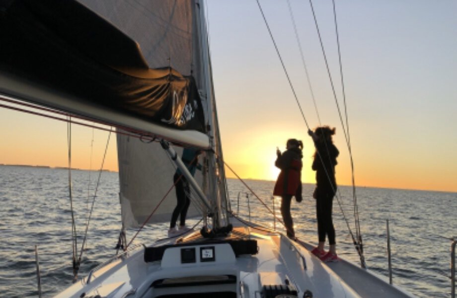 Zeilboot met twee personen, op de achtergrond ondergaande zon