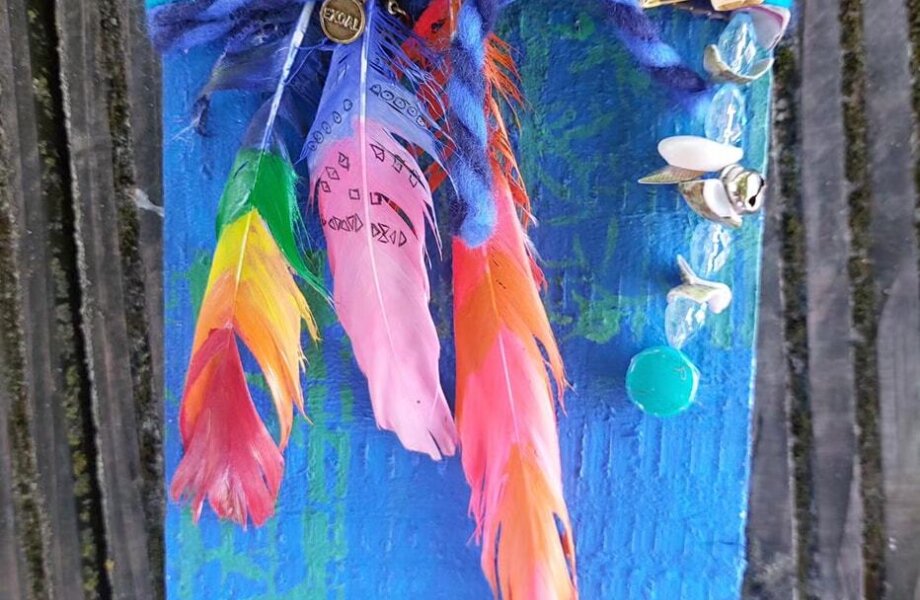 Bordje van hout met versieringen onder andere veren, kralen, wol