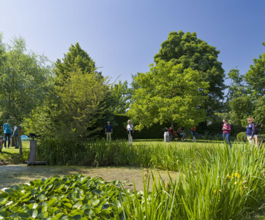 Mensen bekijken beelden in een tuin in Wemeldinge tijdens de Kunst- en Natuurroute